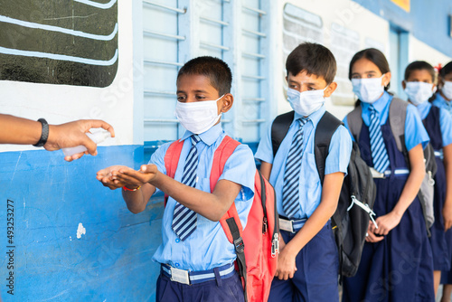 School kids with medical face mask being test with temperature and applying sanitizer before entering to class - concept of coronavirus covid-19 precautions, healcare measures and back to school. photo