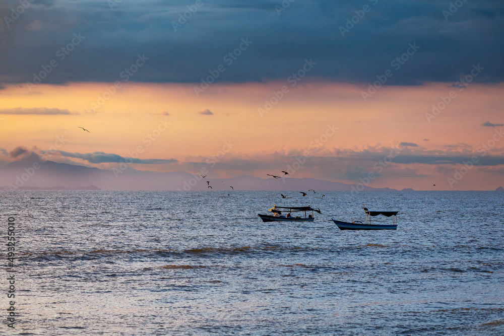 Fototapeta premium Evening view of the Pacific Coast in Tarcoles, sunset, glittering waves and fisherman boats. Idyllic sunset landscape. Tarcoles, Costa Rica. Pura Vida concept, travel to exotic tropical country.