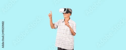  old Asian man playing VR video game with virtual reality goggles and Shock and surprise face ,trying to touch something on light blue background in studio With copy space.