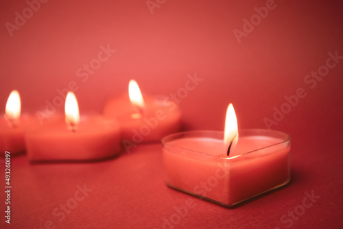 Red burning heart-shaped candles with blazing flames. Tongues of fire on a red background. Valentine's Day, passion, love, feelings, romantic mood concept. Monochrome wallpaper. Decor for February 14.