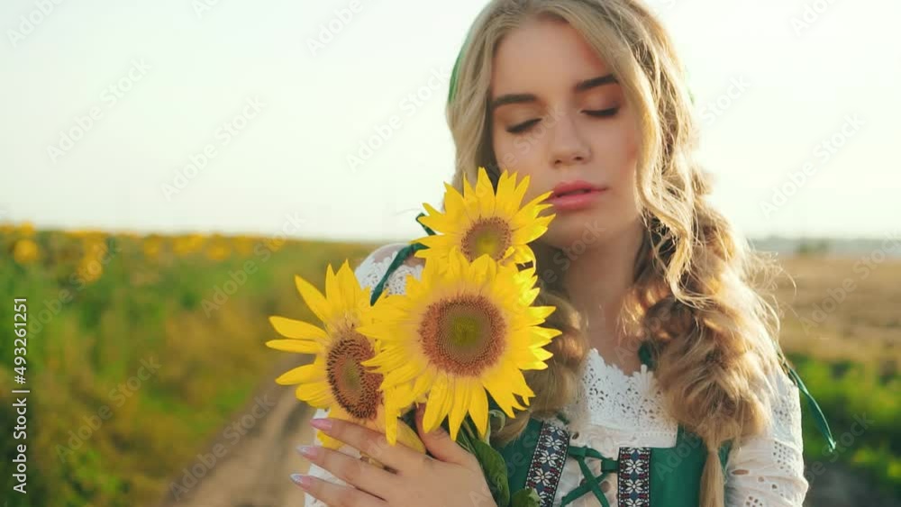 Ukrainian authentic young beautiful blonde woman holding embrace hug bouquet yellow sunflowers. Green national traditional dress. Backdrop bright sun flare, sky, flowering field. Sad pretty face Ukrainian authentic young beautiful blonde woman holding embrace hug bouquet yellow sunflowers. Green national traditional dress. Backdrop bright sun flare, sky, flowering field. Sad pretty face