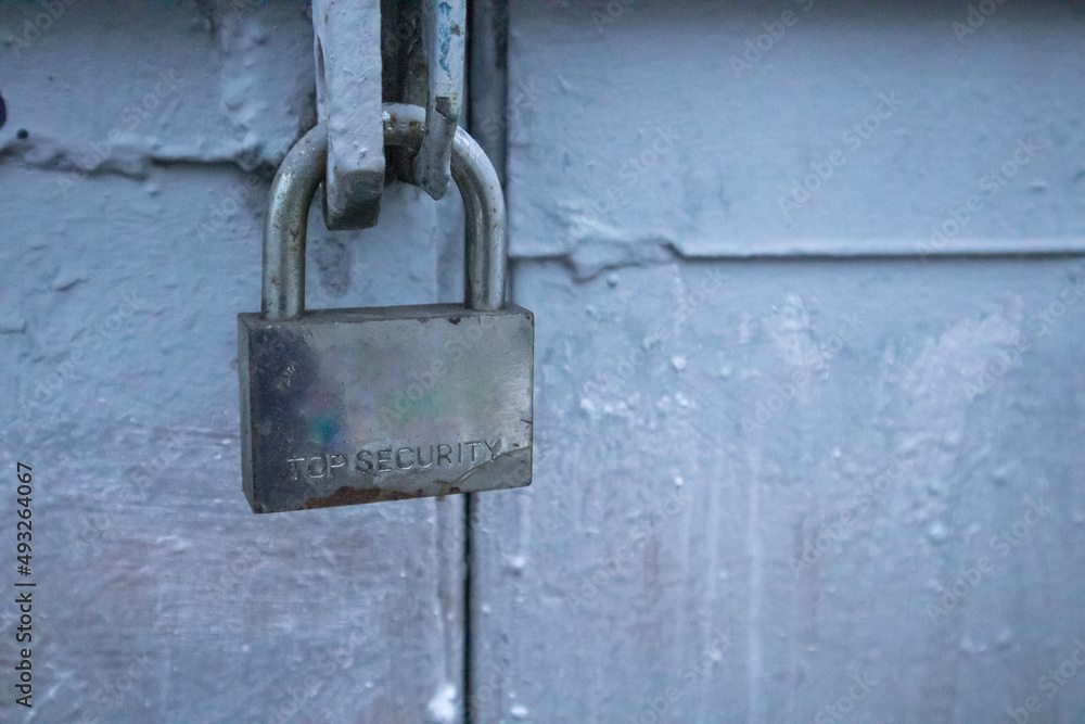A metal lock with engraved text Top Secret hangs on the blue garage door. Protection of the house or other property from burglars, thieves. Private territory. Locked up door from outdoors. A padlock.