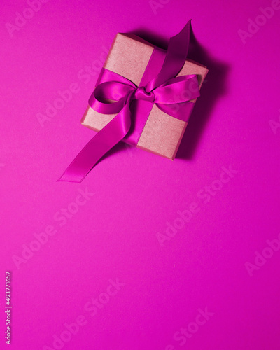Brown paper gift box with a dark pink satin ribbon bow on pink background at the bottom with copy space. Flat lay Valentines day father mother day and presents concept.