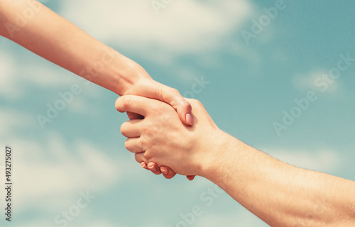 Hands of man and woman reaching to each other, support. Giving a helping hand. Lending a helping hand. Solidarity, compassion, and charity, rescue. Hands of man and woman on blue sky background © Yevhen