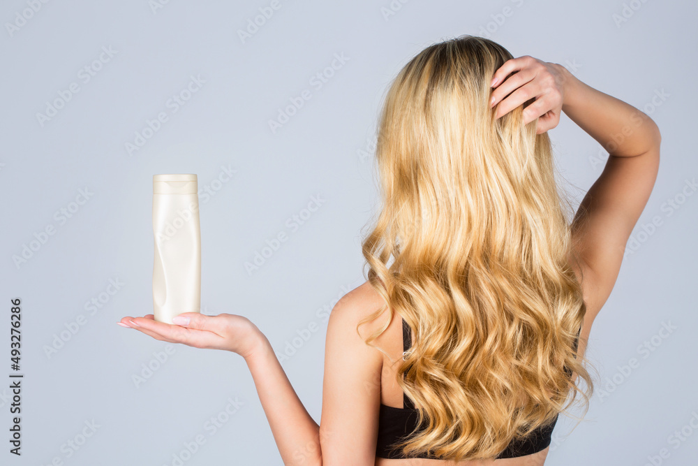 Woman long hair. Woman hold bottle shampoo and conditioner. Woman holding shampoo bottle. Beautiful blonde girl with a bottle of shampoos in hands. Girl with shiny and long hair - obrazy, fototapety, plakaty 