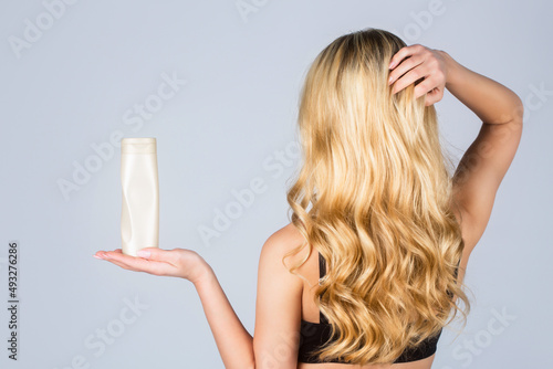 Woman long hair. Woman hold bottle shampoo and conditioner. Woman holding shampoo bottle. Beautiful blonde girl with a bottle of shampoos in hands. Girl with shiny and long hair