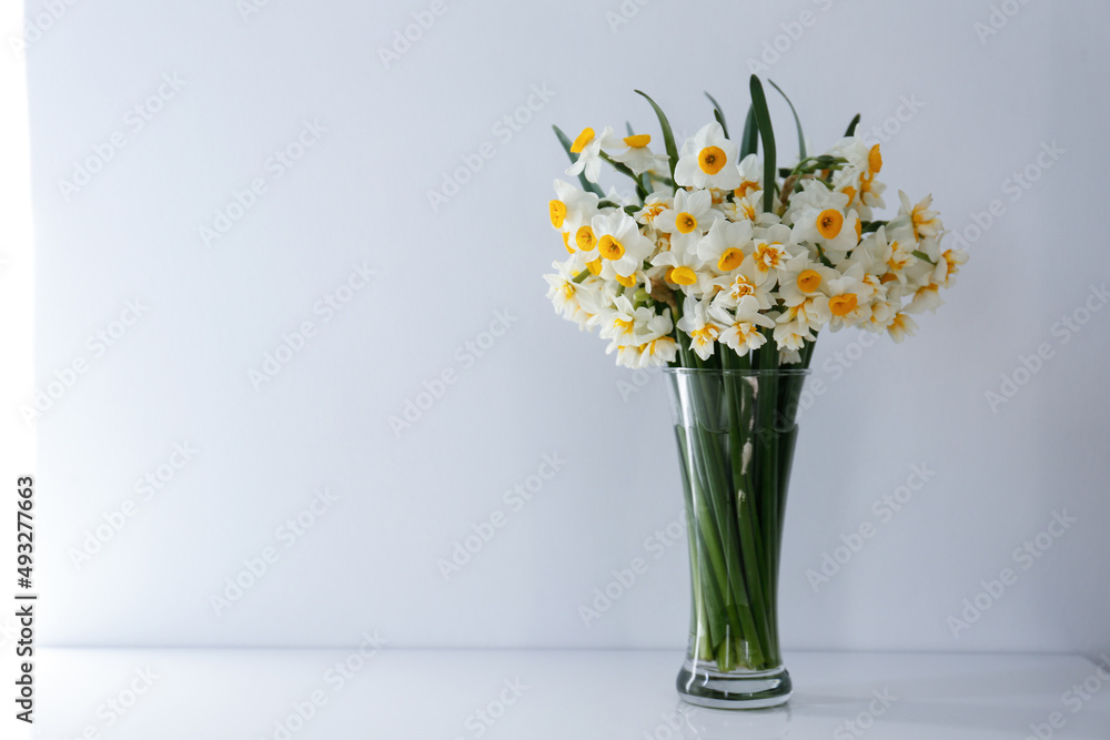 A bouquet of white daffodils in glass vase on the table, natural sunlight. Narcissus flowers in minimal close up composition with visible petal texture. Background, copy space top view. A bouquet of white daffodils in glass vase on the table, natural sunlight. Narcissus flowers in minimal close up composition with visible petal texture. Background, copy space top view.