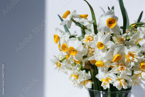 A bouquet of white daffodils in glass vase on the table, natural sunlight. Narcissus flowers in minimal close up composition with visible petal texture. Background, copy space top view.