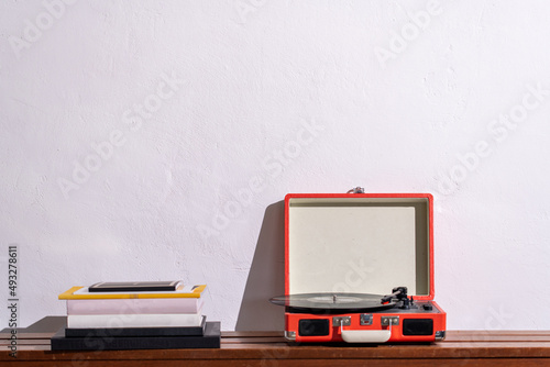 Pile of books and a retro turntable on a wooden shelf against a white wall. Record player. High quality photo