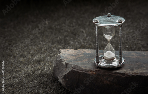 Silver hourglass or Sandglass on Huge stone over grass background. Hope and Value of time concept, Copy space, Selective focus. © num
