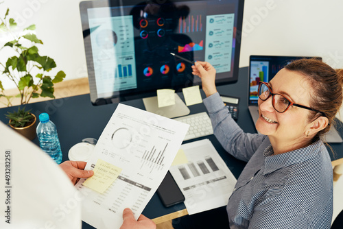 Woman entrepreneur discussing financial data with her colleague sitting at desk in office. Happy positive businesswoman working with charts and tables on computer. Two people working together