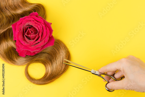 A hand holds a hairdressing tool over brown hair on a yellow background. Hair care and beauty products.