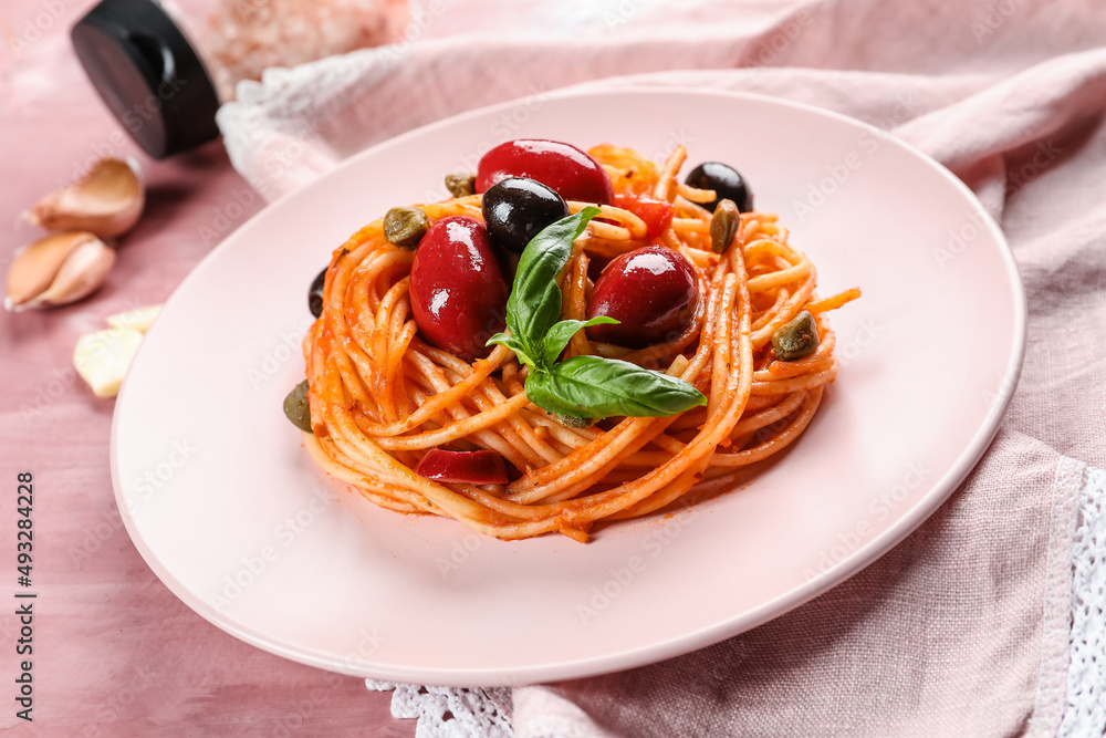Plate with tasty Pasta Puttanesca on pink background Plate with tasty Pasta Puttanesca on pink background