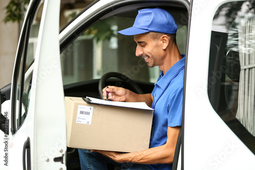 Male courier of delivery company with parcel in automobile