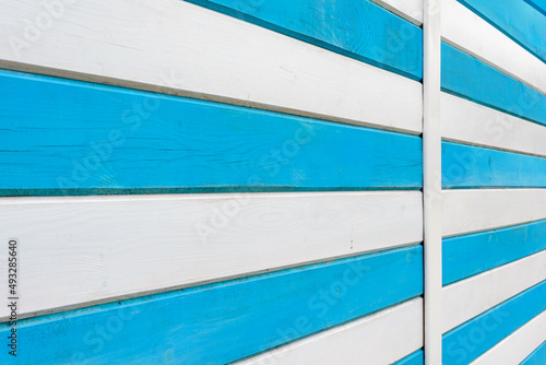 Striped wooden beach fence. View in perspective. Blue and white fence on the beach. Wooden structures