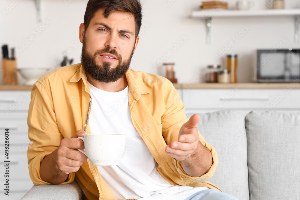Handsome young man with cup of tea video chatting in kitchen Handsome young man with cup of tea video chatting in kitchen
