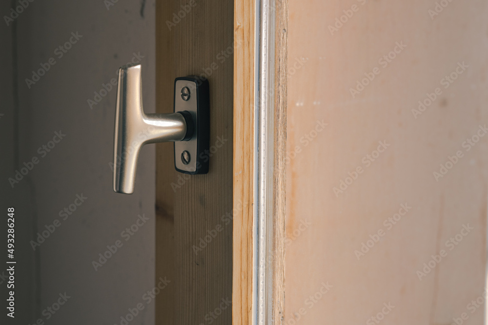 Typical window knob mounted on a wooden window frame in closed position. Metal contemporary modern knob or hook for opening the window.