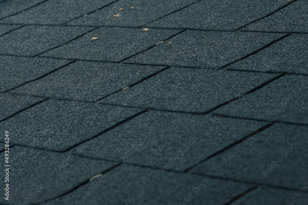 Obraz premium Bitumen roof tiles on a roof stacked together on an already worn out roof.