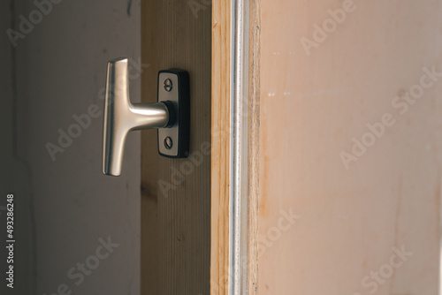 Typical window knob mounted on a wooden window frame in closed position. Metal contemporary modern knob or hook for opening the window. © Anze