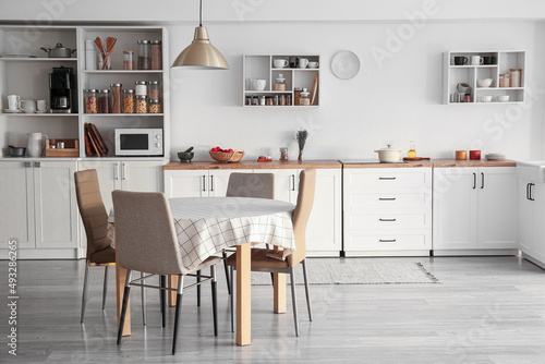 Interior of light modern kitchen with white counters, dining table and shelves © Pixel-Shot