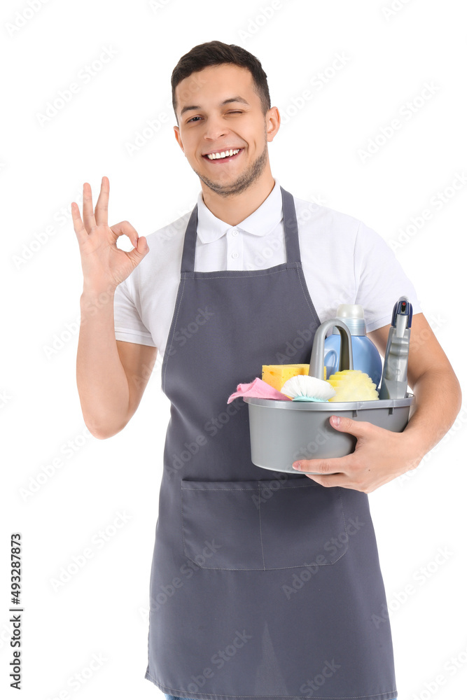 Young male worker of cleaning service with supplies in bucket showing OK on white background Young male worker of cleaning service with supplies in bucket showing OK on white background