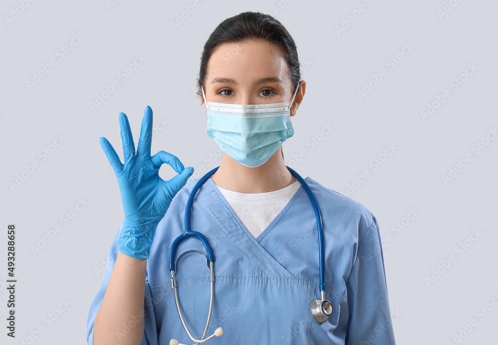 Portrait of female doctor showing OK on grey background Portrait of female doctor showing OK on grey background