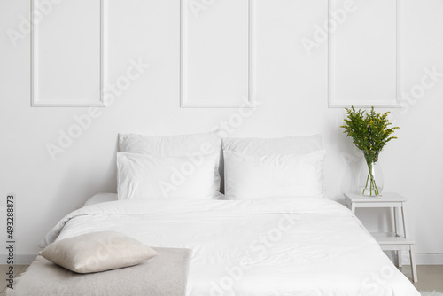 Comfortable bed and vase with flowers on stepladder near white wall © Pixel-Shot