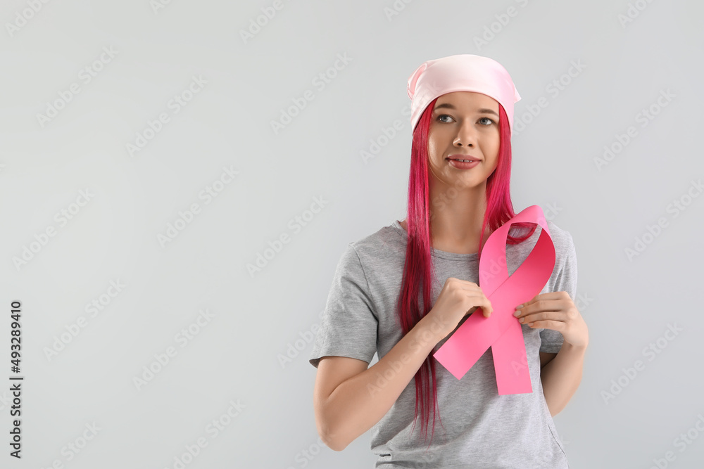 Young woman with pink ribbon on light background. Breast cancer awareness concept Young woman with pink ribbon on light background. Breast cancer awareness concept
