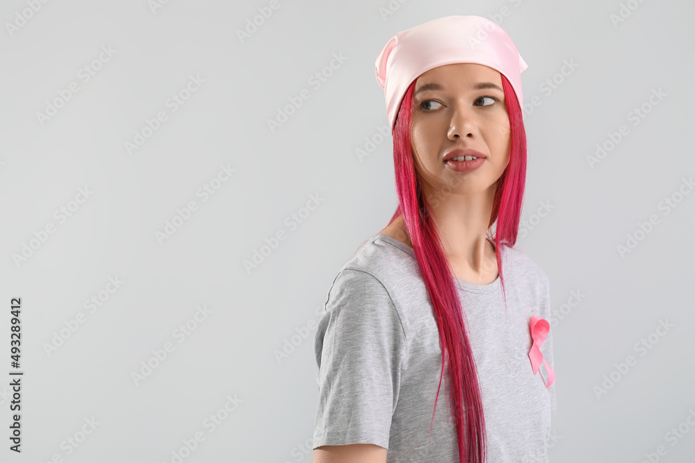Young woman with pink ribbon on light background. Breast cancer awareness concept Young woman with pink ribbon on light background. Breast cancer awareness concept