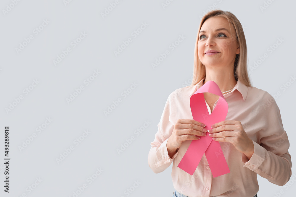 Woman holding pink awareness ribbon and looking aside on light background. Breast cancer awareness concept Woman holding pink awareness ribbon and looking aside on light background. Breast cancer awareness concept