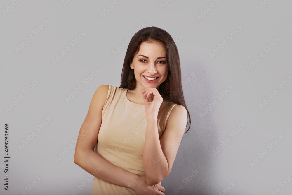 Beautiful happy businesswoman looking with hand under the face in casual beige clothing on light grey background with empty copy space. Beautiful happy businesswoman looking with hand under the face in casual beige clothing on light grey background with empty copy space.