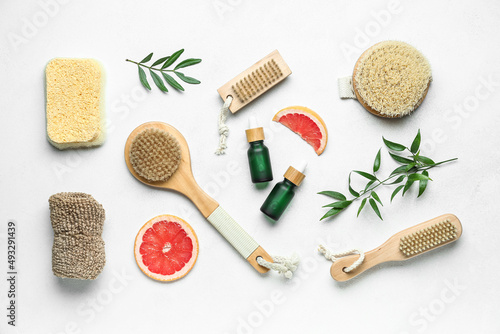 Bottles of grapefruit oil with bathing supplies on light background