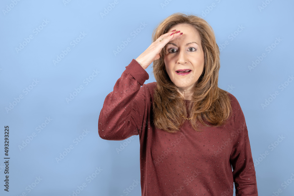 Woman with a surprised face and hand on the forehead for emotion, blue studio background.