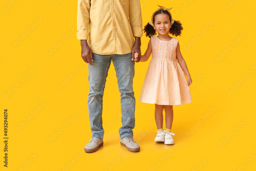 Little African-American girl and her father on yellow background