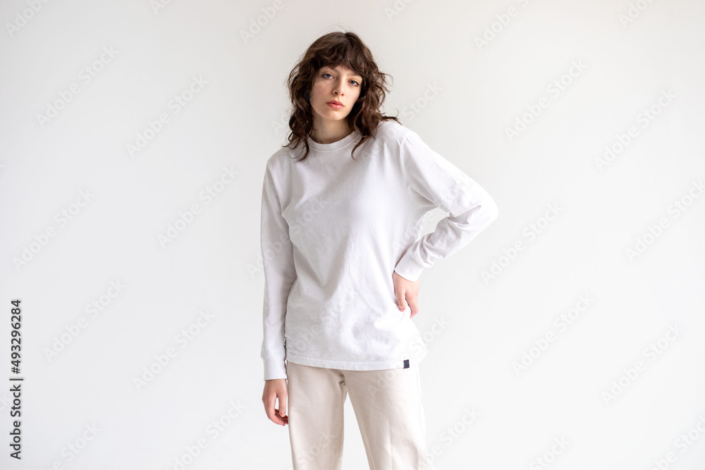 Young woman with curly hair in a white long sleeve t-shirt stands on a white background. Mock-up.