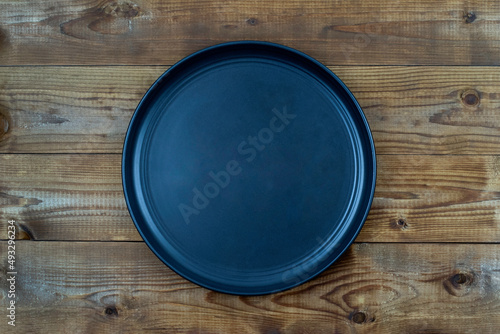 Black ceramic plate on dark brown wooden table background , top view. Menu concept