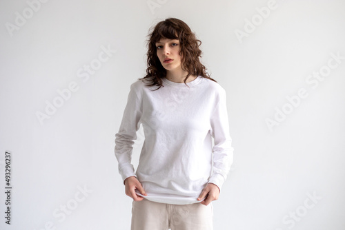 Young woman with curly hair in a white long sleeve t-shirt stands on a white background. Mock-up.
