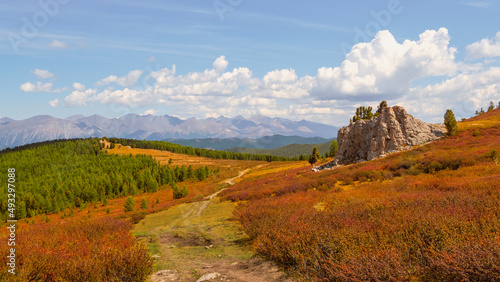 Panoramic view of broken dirt road through the summer plateau. Awesome alpine scenery with beautiful big rock in golden sunshine in autumn colors.