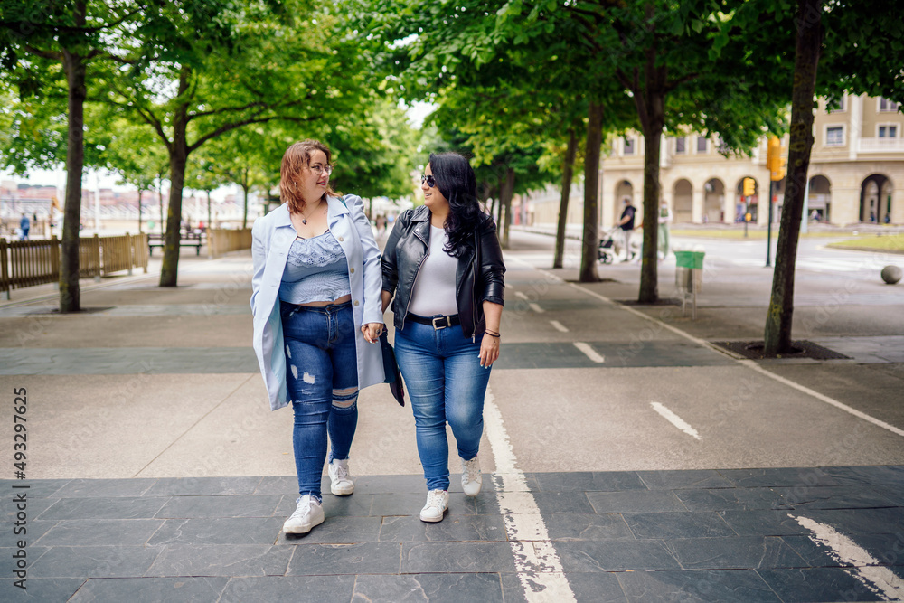 Plus size girlfriends holding hands and walking in city Plus size girlfriends holding hands and walking in city