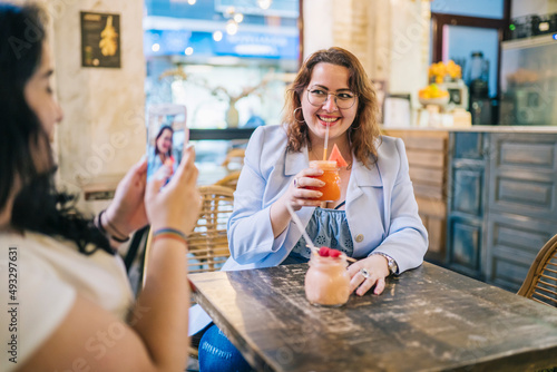 Smiling lady photographing friend drinking juice in bar photo