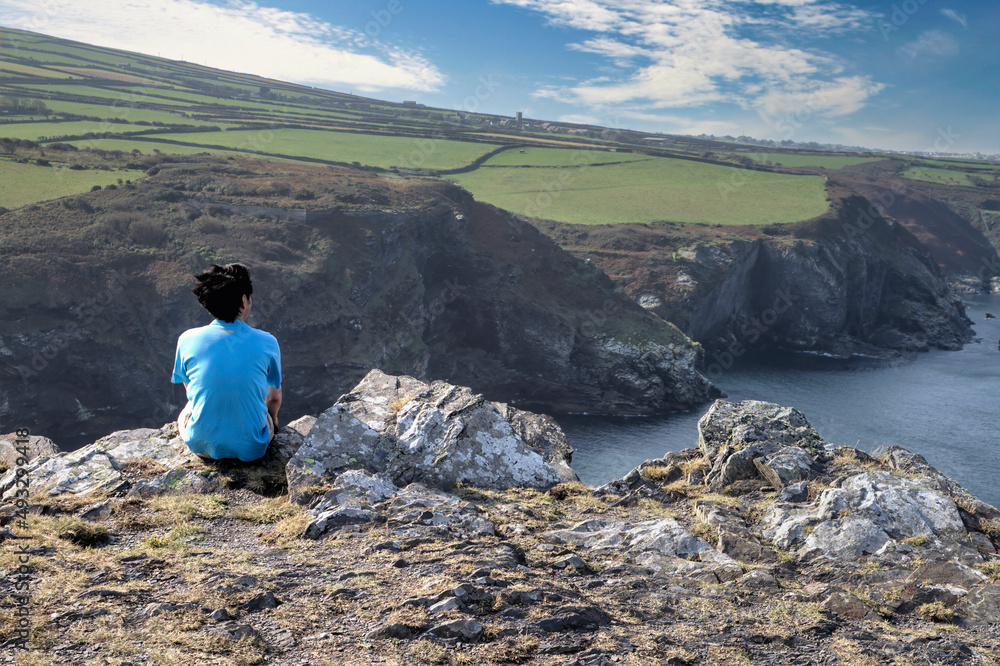 A man sitting on a rocky ridge, Boscastle, Cornwall, UK. A man sitting on a rocky ridge, Boscastle, Cornwall, UK.