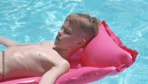 Young joyful child boy having fun swimming on inflatable air mattress in swimming pool with blue water on warm summer day on tropical vacations. Summertime activities concept