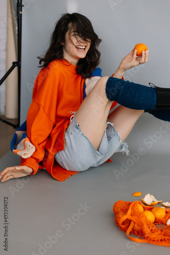 stylish woman dressed in orange knitted jacket posing for a photo in a photo studio on a gray paper background. Bright emotions, poses, modern concept