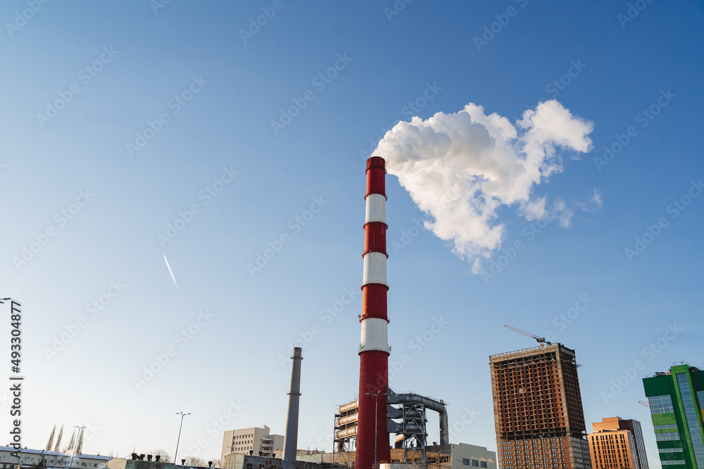 The city is polluted by harmful emissions coming out of the pipes of the plant. The carbon footprint falls on buildings, climate warming, a pipe against the sky.