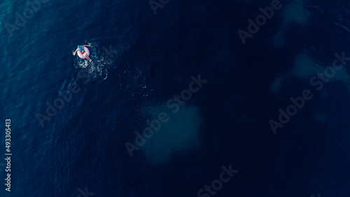 Aerial view of young brunette woman swimming on the inflatable big donut in the blue sea. Top view of slim lady relaxing on her holidays Adriatic sea.