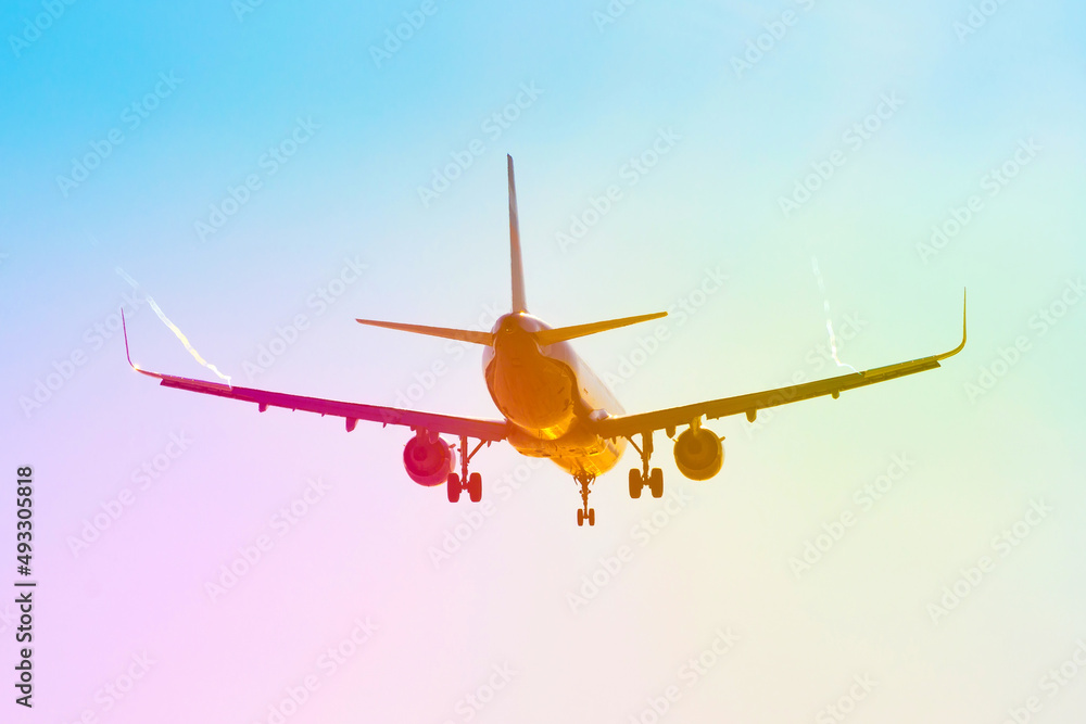 Passenger airplane flies near the sun glare with a color rainbow gradient on landing, with the wings of a steam jet vortex. Passenger airplane flies near the sun glare with a color rainbow gradient on landing, with the wings of a steam jet vortex.