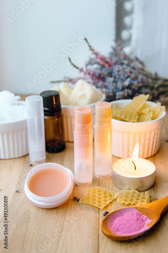 Ingredients for homemade lip balm: shea butter, essential oil, mineral color powder, beeswax, coconut oil. Homemade lip balm lipstick mixture with ingredients scattered around.