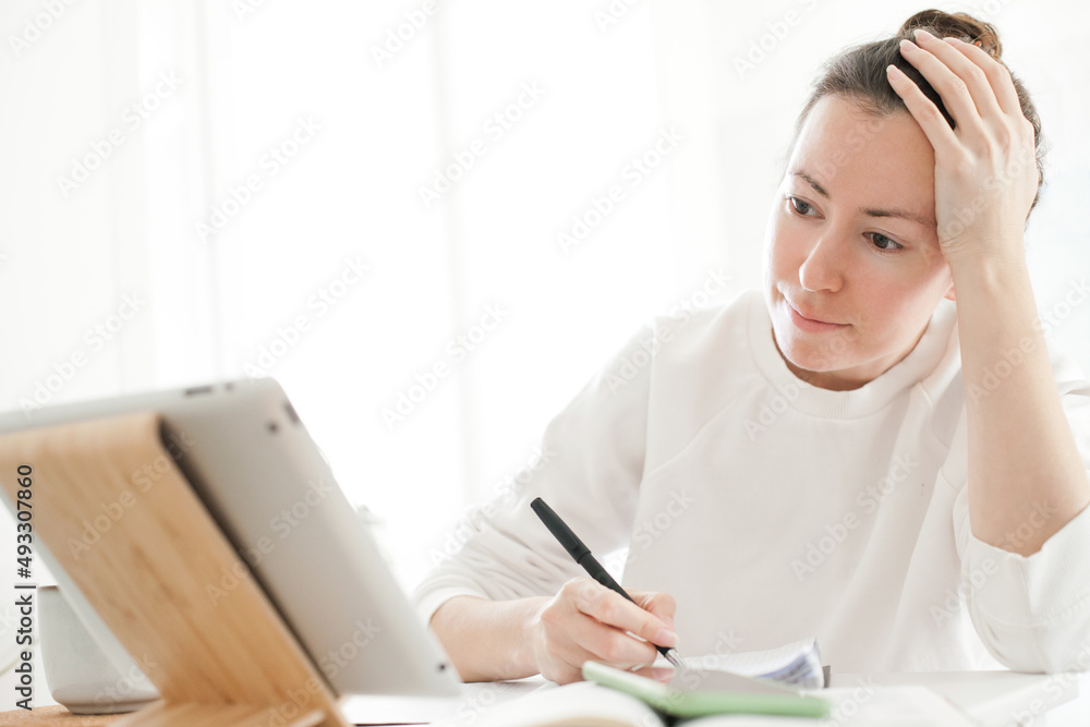 Young woman studying online with tablet or laptop and writing down notes. Online education for young people at home - studying on a distance via internet Young woman studying online with tablet or laptop and writing down notes. Online education for young people at home - studying on a distance via internet