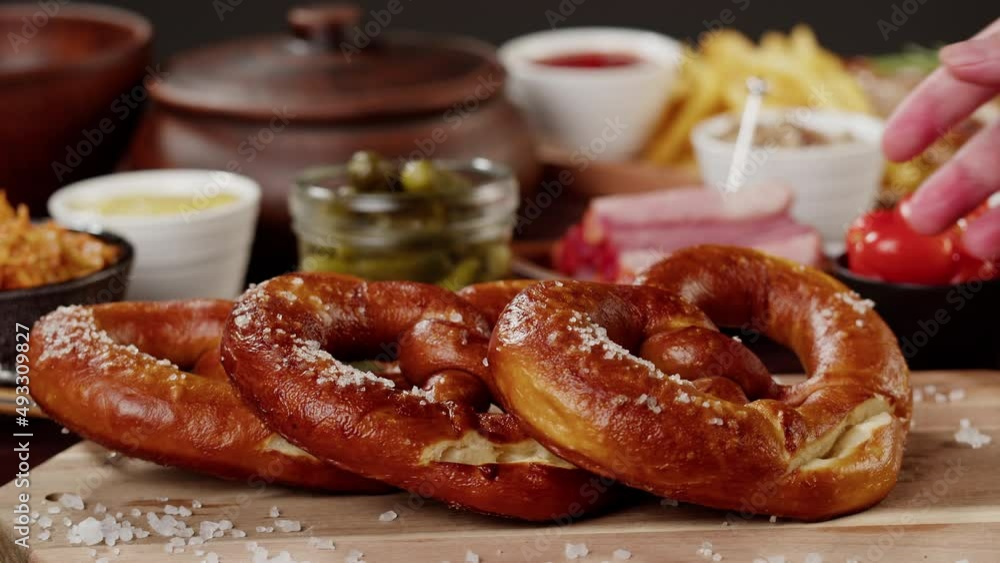 Putting fresh baked pretzel close-up. Traditional German Cuisine. Smoked sausages with fried potatoes, pickled cucumbers, bratwursts on table. Composition of Cooked National Czech Food. Putting fresh baked pretzel close-up. Traditional German Cuisine. Smoked sausages with fried potatoes, pickled cucumbers, bratwursts on table. Composition of Cooked National Czech Food.