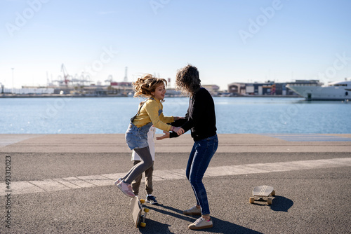 Mother helping girl jumping on skateboard near sed photo